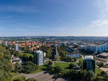 Panorama Plauen Wohnungsbau Das Bild zeigt eine Panoramaaufnahme einer Stadtlandschaft bei Tageslicht. Der Himmel ist klar und blau, die Sonne steht hoch oben rechts im Bild.