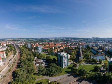 Panorama Plauen Wohnungsbau Das Bild zeigt eine Panoramaaufnahme einer Stadtlandschaft bei Tageslicht. Der Himmel ist klar und blau, die Sonne steht hoch oben rechts im Bild.