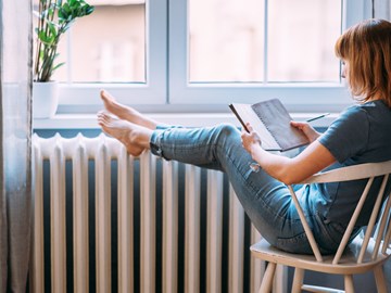 Frau mit Buch legt Beine auf einen Heizkörper Frau mit Buch legt Beine auf einen Heizkörper