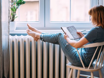 Frau mit Buch legt Beine auf einen Heizkörper Frau mit Buch legt Beine auf einen Heizkörper
