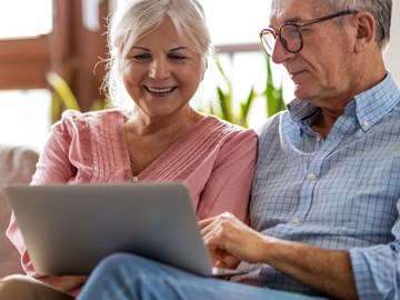 Frau und Mann schauen auf dem Laptop in das Kundenportal Frau und Mann sitzen auf dem Sofa vor dem Fenster und schauen auf dem Laptop in das Kundenportal