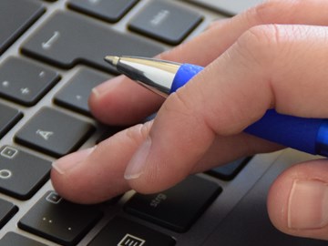 Nahaufnahme einer Hand mit Kugelschreiber auf der Tastatur Nahaufnahme einer Hand mit Kugelschreiber auf der Tastatur
