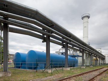 Außenaufnahme des Heizkraftwerks Guben, im Vordergrund ein Versorgungsrohrsystem und blaue Tanks Außenaufnahme des Heizkraftwerks Guben, im Vordergrund ein Versorgungsrohrsystem und blaue Tanks