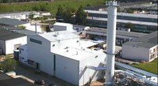 Heizkraftwerk Guben Das Foto zeigt eine industrielle Anlage mit mehreren Gebäuden. Im Mittelpunkt steht ein großes weißes Gebäude mit einem hohen, zylindrischen Schornstein oder Abluftrohr.