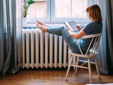Frau mit Buch legt Beine auf einen Heizkörper Frau mit Buch legt Beine auf einen Heizkörper